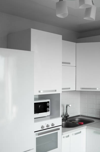 istock Comfortable white kitchen with a white lacquered facades. Modern kitchen clean interior design. Refrigerator, kitchen oven, microwave oven and sink. Kitchen supplies. 1293316056