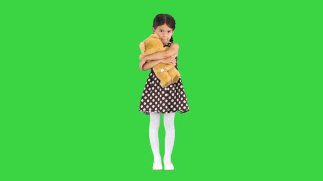 Little girl in polka dot dress hugging teddy bear really tight smiling at camera on a Green Screen, Chroma Key