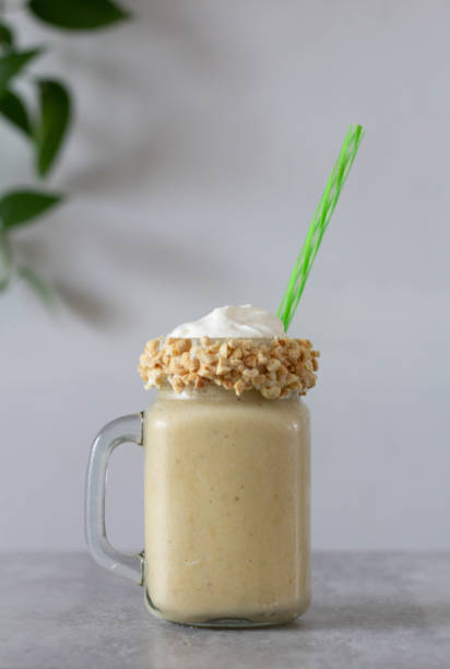 Banana and peanut butter smoothie in a glass jar mug with handle and nuts along the edge