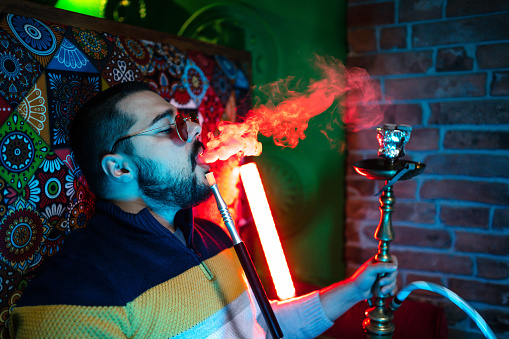 Young man enjoying while smoking hookah in a bar
