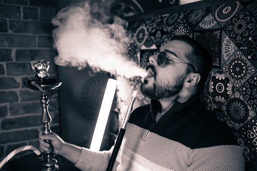 Young man enjoying while smoking hookah in a bar
