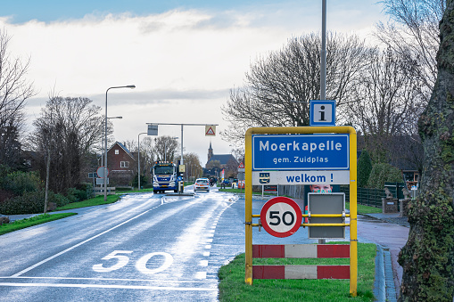 Moerkapelle, Netherlands - December 2020: Place name sign of Moerkapelle, a village in the western part of Holland. In the background the tall church in the centre of the village can be seen.