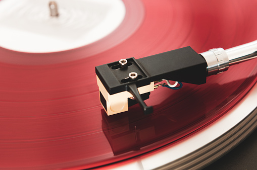 Close-up of a record player playing a red colored vinyl. Focus is on the cartridge.