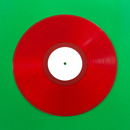 Close-up of a red vinyl record on green background. The white label can be used as copy space.