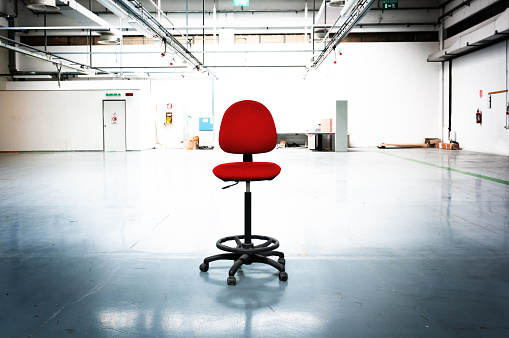 Empty industrial space with an old red office chair in the middle. Toned dimage.