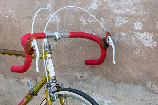 Vintage racing bicycle with red handlebars, leaning against a ruined concrete wall.