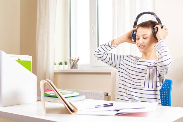 istock Kid with tablet computer sitting at table with books and having video call, virtual online lesson at home 1293335754