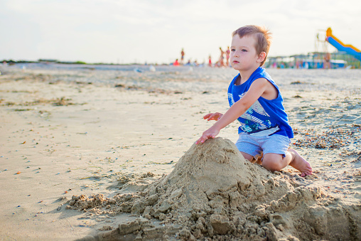 A little cute baby boy is playing on a beach near a sea. Boy building sandcastle on the beach