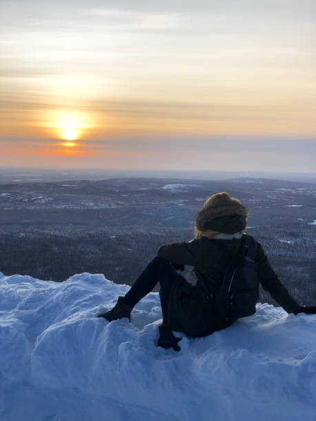 A young woman sits on the top of a mountain and admires the sunset. Snow-covered ski slope of Lapland. Snowy, winter landscape and a lot of snow. A young woman sits on the top of a mountain and admires the sunset. Snow-covered ski slope of Lapland. Snowy, winter landscape and a lot of snow. Photo by smartphone. norrbotten province stock pictures, royalty-free photos & images