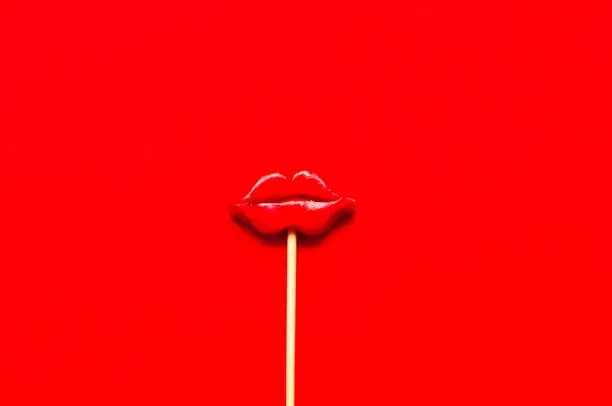 Photo of Creative layout with  with lips on stick. Valentine day concept or World Kiss Day. Festive red background.