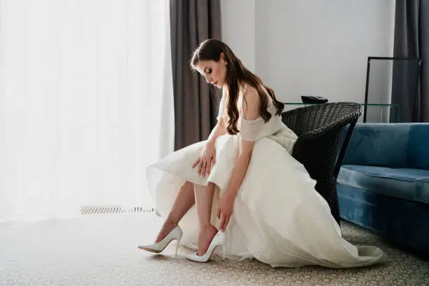 Photo of A beautiful bride puts on shoes. Preparing for the wedding ceremony.