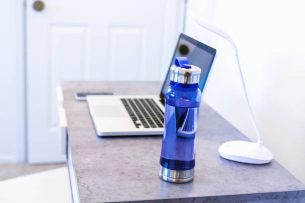 Laptop Water Bottle and Lamp on Desk In Western Colorado Laptop Water Bottle and Lamp on Desk (Shot with Canon 5DS 50.6mp photos professionally retouched - Lightroom / Photoshop - original size 5792 x 8688 downsampled as needed for clarity and select focus used for dramatic effect) bottled water on table stock pictures, royalty-free photos & images