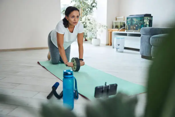 Serious strong young woman grasping the handles of an abdominal roller with an overhand grip