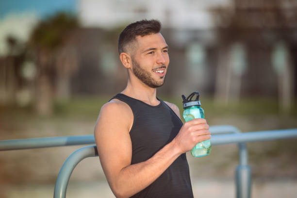 istock Young fitness man drinking water with lemon from reusable bottle during a workout. Drinking while exercising. Dehydration while training 1293364238