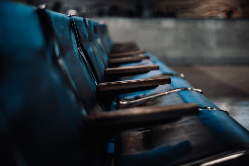 A row of empty leather old-fashion seats in a dark waiting hall of an old domestic airport with shallow depth of field and selective focus on a wooden armrest in the middle, bluish tint