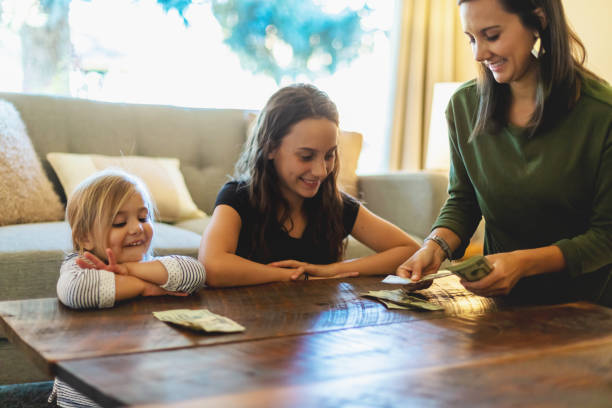 Millennial Female Mother with Teenage and Pre School Age Daughters Handling Money In Western Colorado Millennial Female Mother with Teenage and Pre School Age Daughters Handling and Counting Money and Passing Our Allowances Training How to budget and be good stewards of resources Photo Series with Matching 4K Video Available (Shot with Canon 5DS 50.6mp photos professionally retouched - Lightroom / Photoshop - original size 5792 x 8688 downsampled as needed for clarity and select focus used for dramatic effect) allowance stock pictures, royalty-free photos & images
