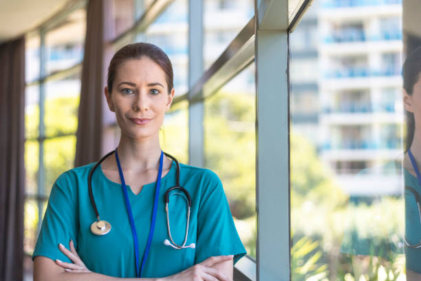 Female doctor in hospital Portrait of a female medical professional confidently looking directly at the camera while standing next to a series of windows in a hospital corridor. self sacrifice stock pictures, royalty-free photos & images