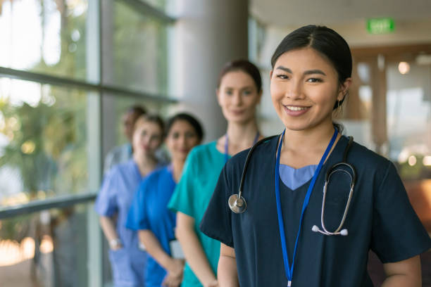 Multi-ethnic team of doctors A female doctor of Asian descent poses with her multi-ethnic team of doctors and nurses and smiles directly at the camera while standing in a hospital corridor. university students australia stock pictures, royalty-free photos & images