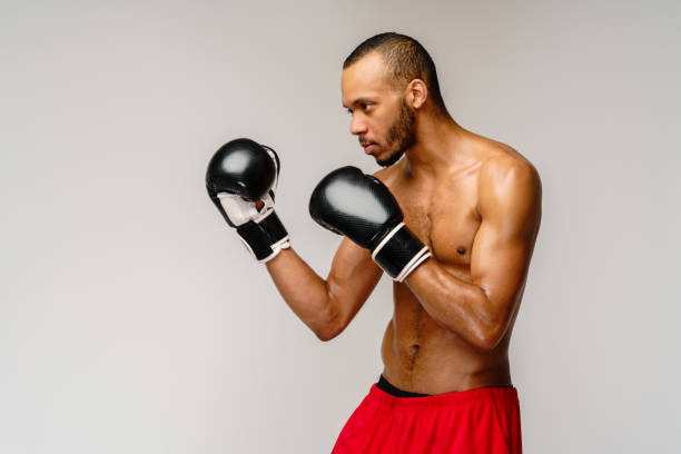 istock Confident young African boxer in boxing gloves standing over light grey background 1293382719