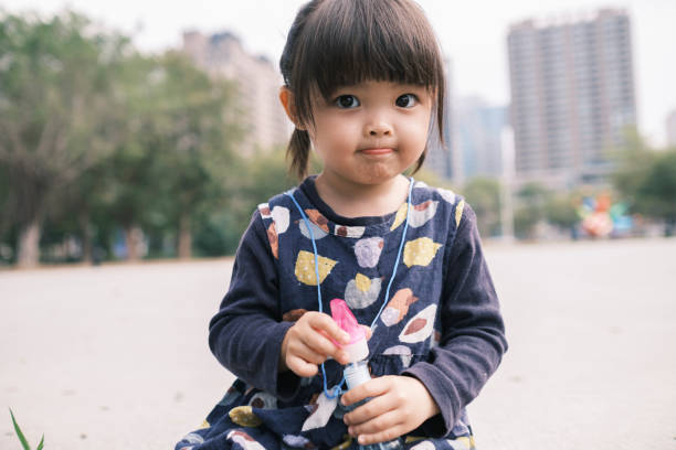 Chinese little daughter blowing bubbles in the park
