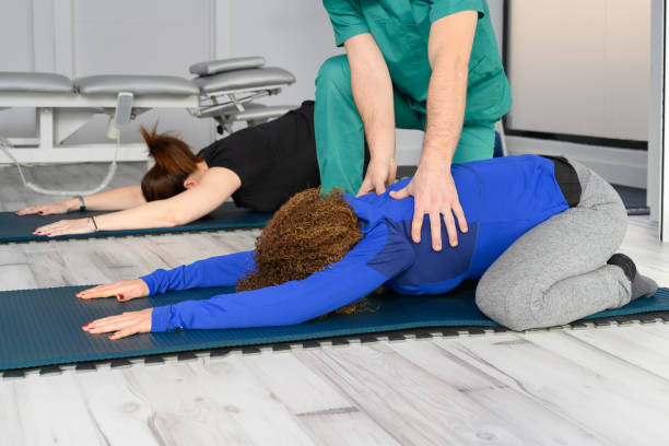 donna che si allena con terapista su tappetino yoga in clinica. foto di alta qualità - yoga men male gymnastics foto e immagini stock
