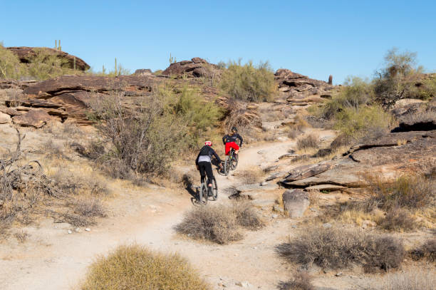Mountain Bikers on Hidden Valley Trail in Hills Above Phoenix Arizona December 20, 2020 - Phoenix, Arizona, USA: Two bikers traverse the Hidden Valley Trail in the desert foothills above Phoenix, Arizona. Nearby is a natural tunnel formed by falling rocks that can be accessed along the trail. phoenix stone stock pictures, royalty-free photos & images
