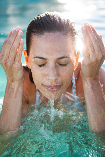bella donna rinfrescante il viso in piscina - splashing color image front view head and shoulders foto e immagini stock