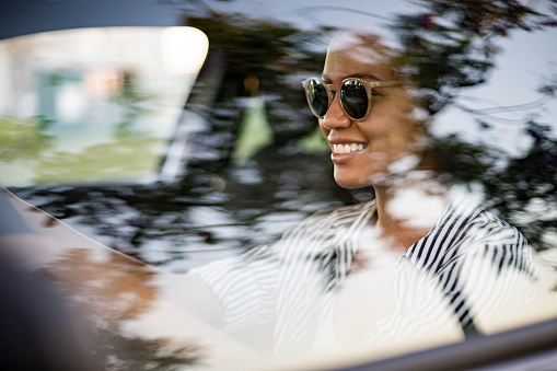 Portrait of smiling woman wearing sunglasses and driving her car during daytime