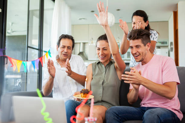 Family having online birthday party Smiling family waving and clapping hands to friends on video call while having a virtual birthday party during covid-19 pandemic virtual birthday celebration stock pictures, royalty-free photos & images