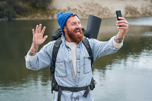 Happy man taking a selfie on the background of nature with a raised hand to the camera as a sign of greeting. Stock photo