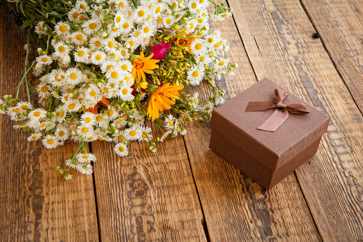 Bouquet of wildflowers and brown gift box on old wooden boards. Top view.
