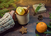 Woman holding a glass of Christmas hot drink with spices on a wooden background with fir branches and Christmas decor. New year's drinks.Traditional hot drink