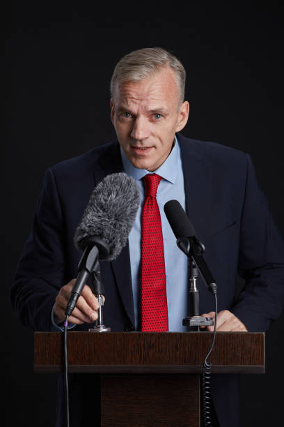 istock Mature Man Speaking to Microphone at Podium 1293444891