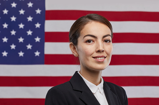 Portrait of smiling female politician looking at camera while standing against USA flag background, copy space