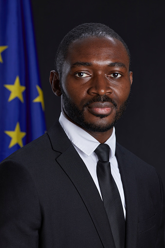 Professional portrait of African-American man looking at camera while standing against EU flag in background