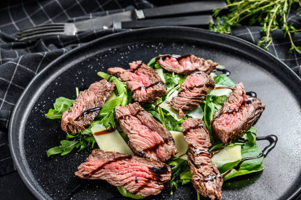 istock Steak salad with spinach, arugula and sliced beef Striploin steak. Black background. Top view 1293446106