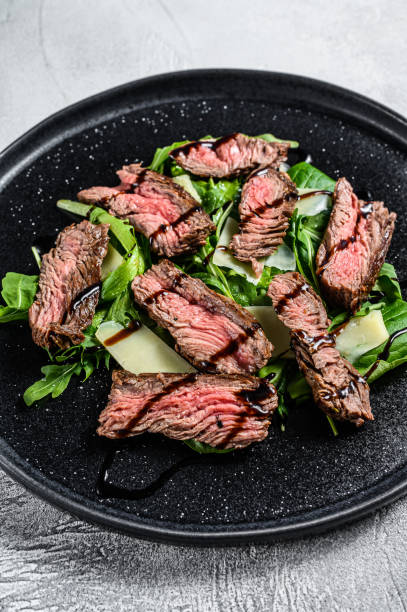 istock Steak salad with spinach, arugula and sliced beef flank steak. Gray background. Top view 1293446125