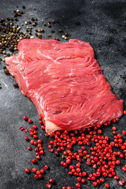 Photo of Raw Flank steak with black and pink pepper. Black background. Top view