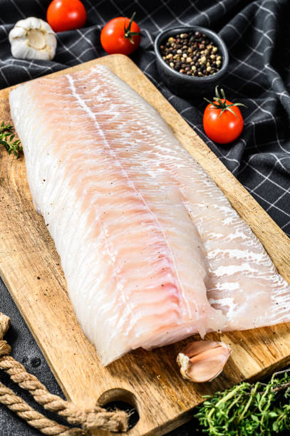istock Raw cod fillet with and herbs on rustic wooden cutting board.  Black background. Top view 1293447819