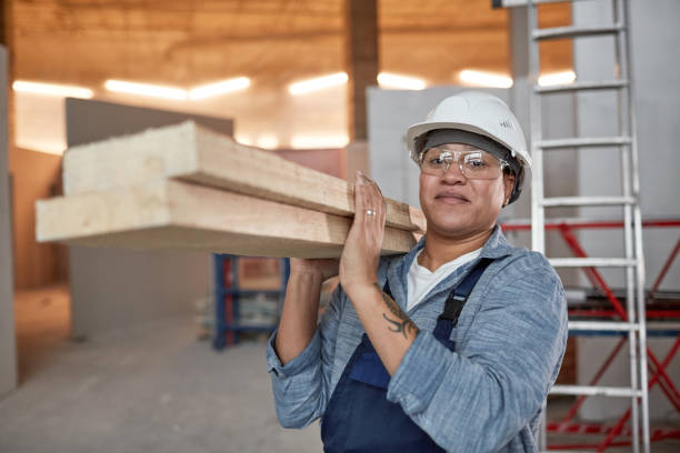 Smiling Female Worker Carrying Wood Waist up portrait of smiling female worker carrying wood boards while working on construction site, copy space construction worker stock pictures, royalty-free photos & images