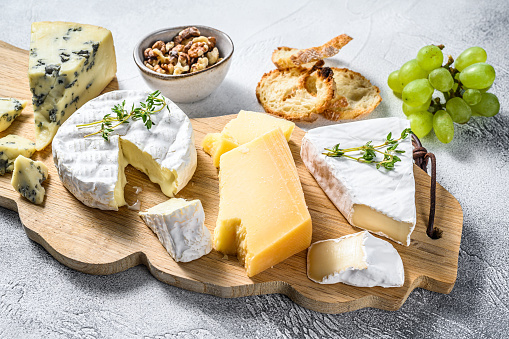 Assorted cheeses on a wooden cutting Board. Camembert, brie, Parmesan and blue cheese with grapes and walnuts. White background. Top view.