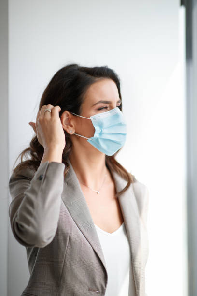 istock Businesswoman standing by the office window with protective face mask 1293452893