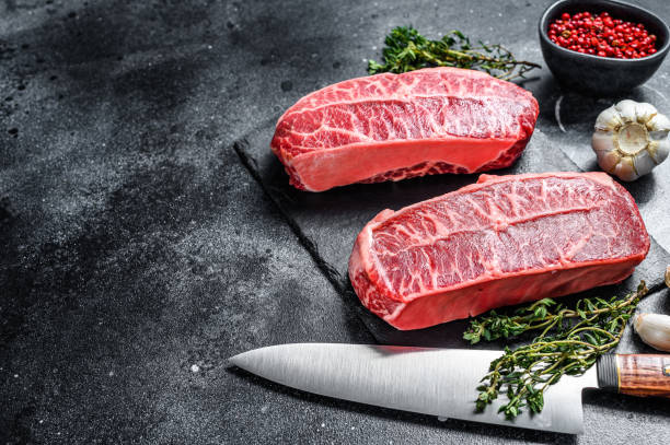 istock Raw top blade steak dry-aged on a stone board. Black background. Top view. Copy space 1293453357