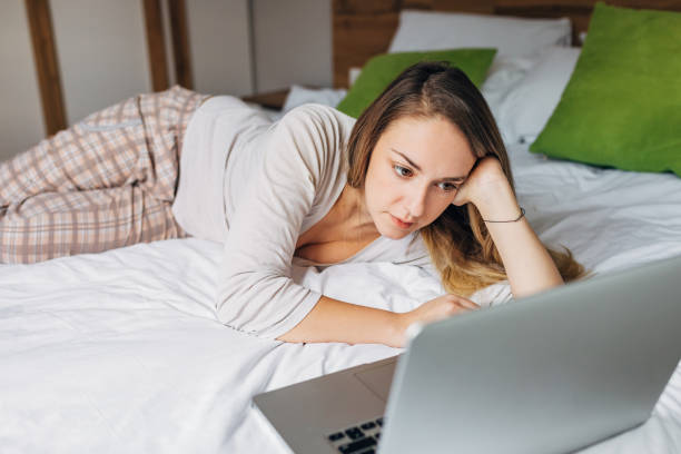 istock Bored female University student, attending an online class via video call from her bed 1293454979