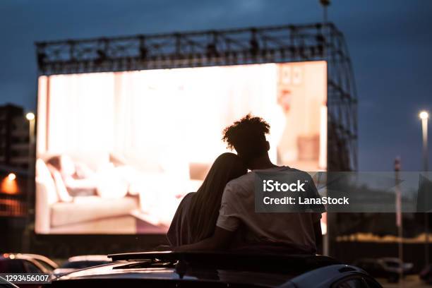 Silhouetted View Of Attractive Young Couple Boy And Girl Embracing Spending Time Together Sitting In The Car While Watching A Movie In A Drive In Cinema Stock Photo - Download Image Now