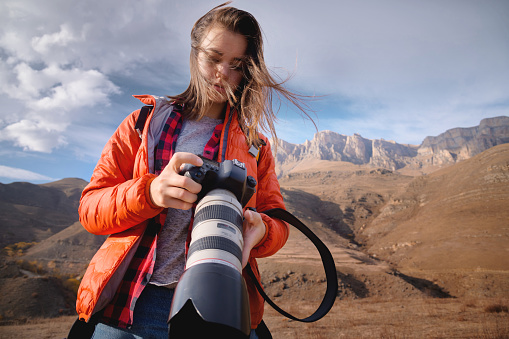 Young attractive caucasian woman with a professional photo camera in her hands against the backdrop of epic high rocks high in the caucasus mountains. Photo tours and landscape photography.