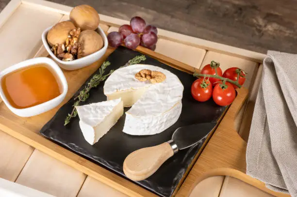 wooden tray for breakfast with brie cheese, honey, walnuts, tomato. cheese breakfast on the wooden tray with black plate