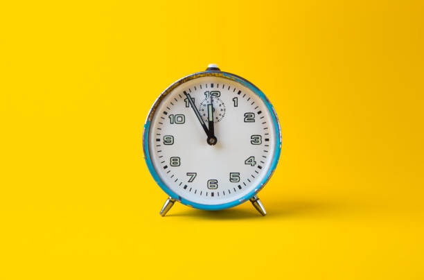 istock Old blue analog clock on a yellow background. It's 11.55 o'clock. 1293459912