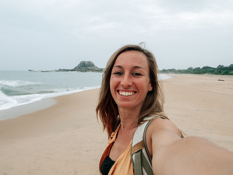 Traveller taking selfie photo by the beach using mobile phone.\nGirl traveling in Sri Lanka