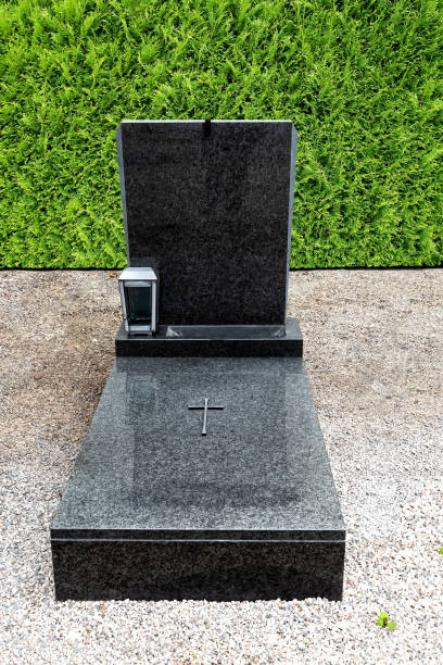 istock Black gravestone with grave border on pebbles with thuja hedge in background 1293469127